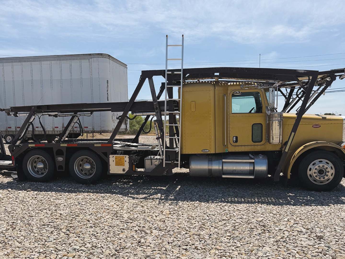 Peterbilt 379 flatbed truck with yellow cab, long car trailer frame, side view showing ladder and exposed frame. No legible labels or serials visible in image.