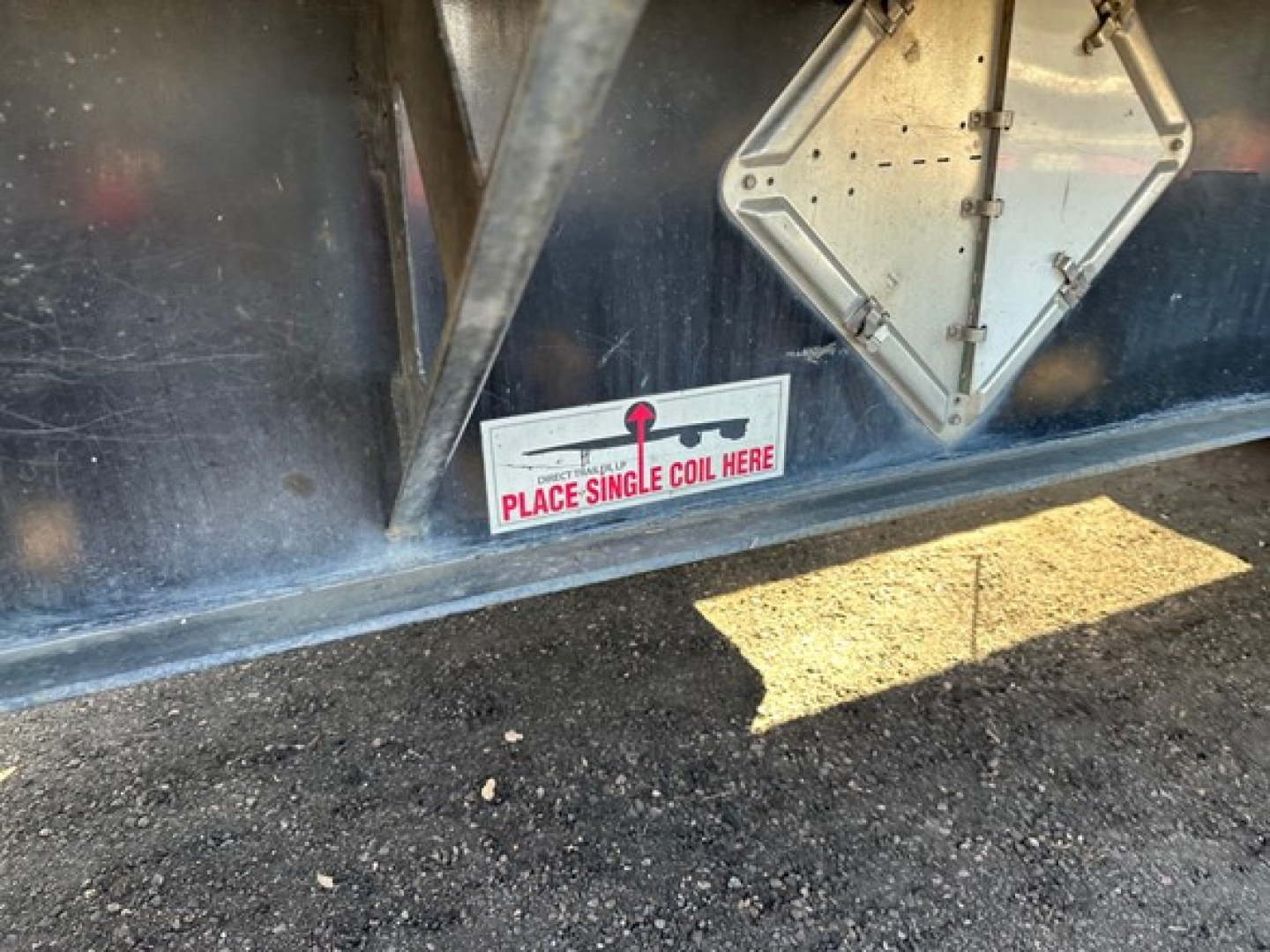Trailer side showing sticker reading PLACE SINGLE COIL HERE and a diamond-shaped access panel on blue steel flatbed