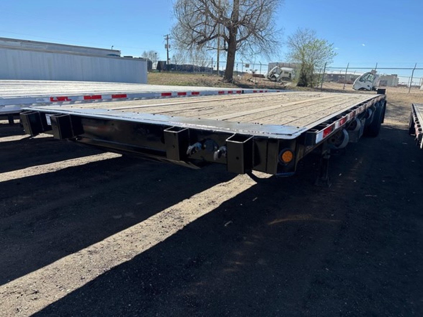 Flatbed trailer showing wooden deck and dual rear axles with taillights and reflectors.