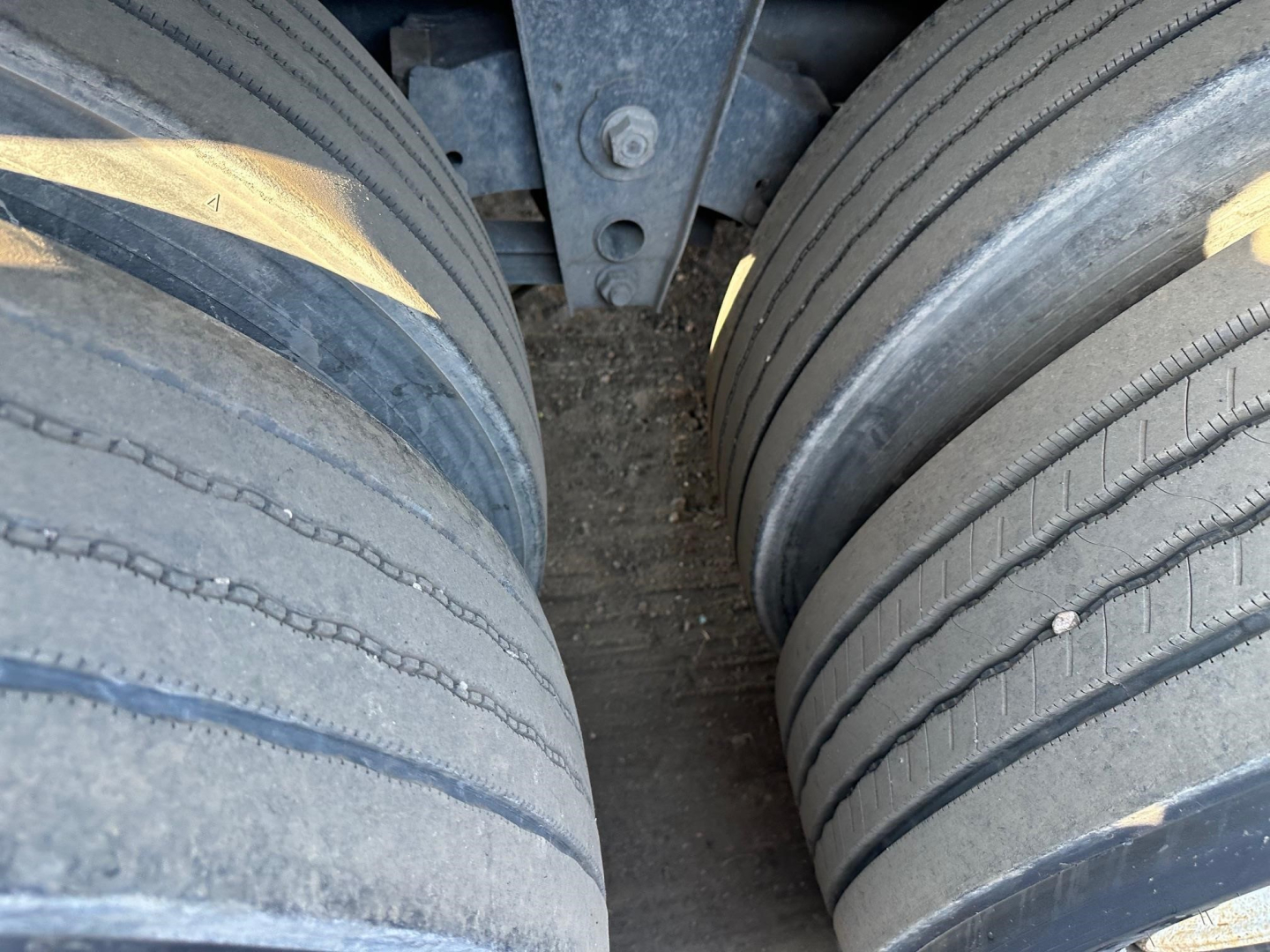 Twin rear trailer tires and undercarriage showing wear marks and frame link; close-up view of tire treads and mud in center.