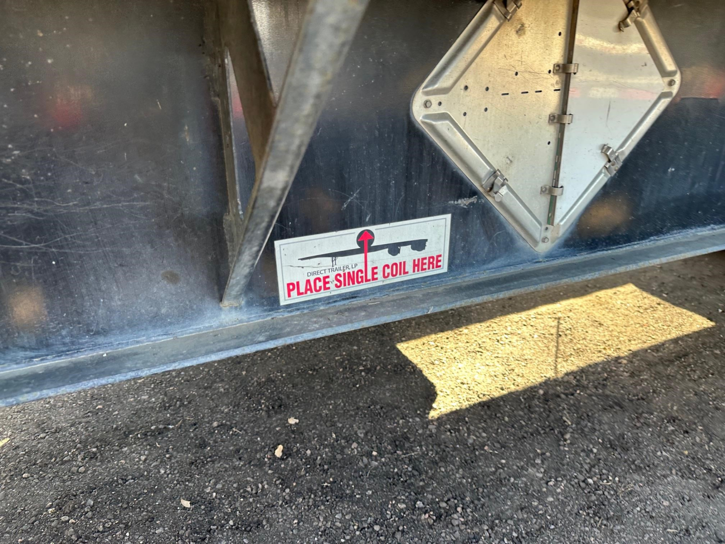 Flatbed trailer side showing a sticker that reads 'Place single coil here' and a diamond-shaped access hatch.