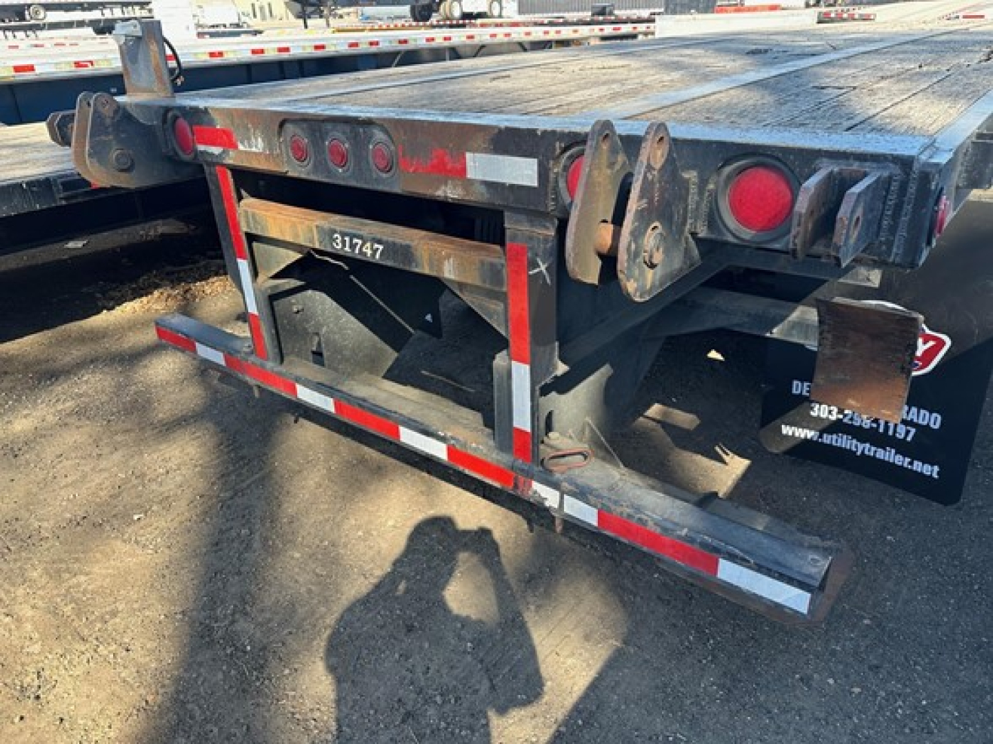 Trailer rear section showing flatbed trailer with hydraulic forklift kit, rear bumper, taillights, and license/stock number plate.