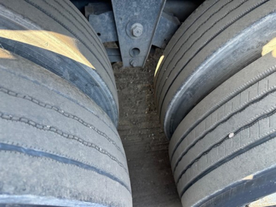 Flatbed trailer axle with dual tires and wheel wells; close-up view of tire treads and hub area.