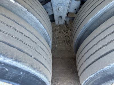 Flatbed trailer wheel view showing dual tires and undercarriage components.