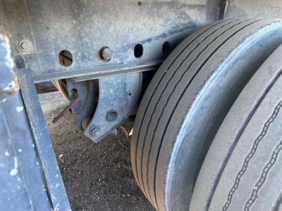 Flatbed trailer wheel and suspension area showing dual tires and blue painted metal frame with bolts and holes.