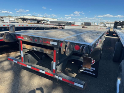 Flatbed trailer showing rear end with taillights, reflective tape, and dark metal deck; visible text on side panels includes contact graphics and numbers.