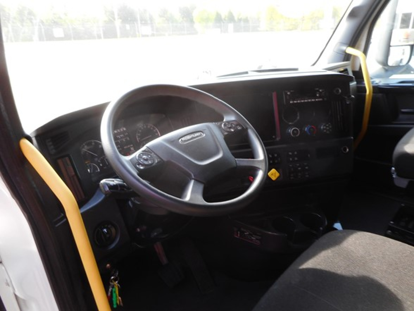 Truck cab interior showing steering wheel and dashboard of Freightliner Cascadia 126, with yellow grab handles and control panels visible.