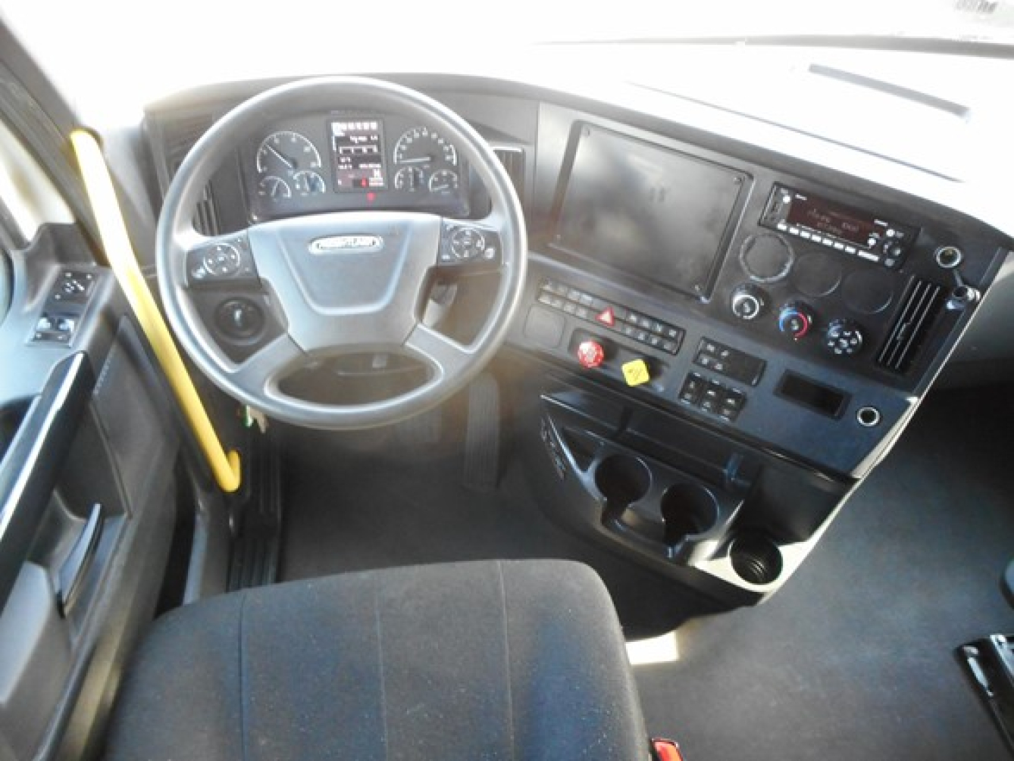 Dashboard and steering wheel of a Freightliner Cascadia 126 truck cab interior with multiple gauges, center console, and touchscreen display.