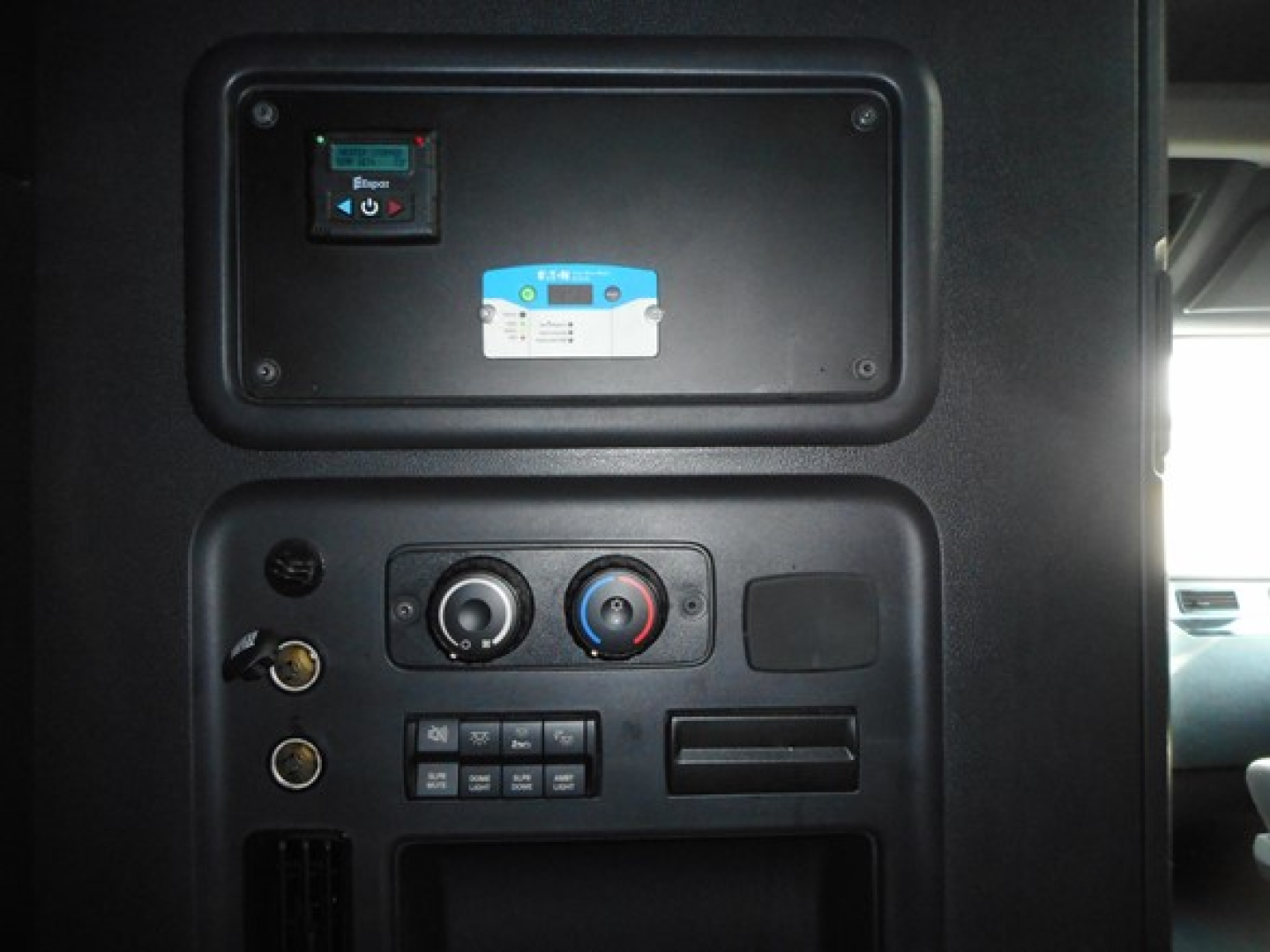 Cab interior control panel of a Freightliner Cascadia showing a breaker panel, climate controls, and switches.