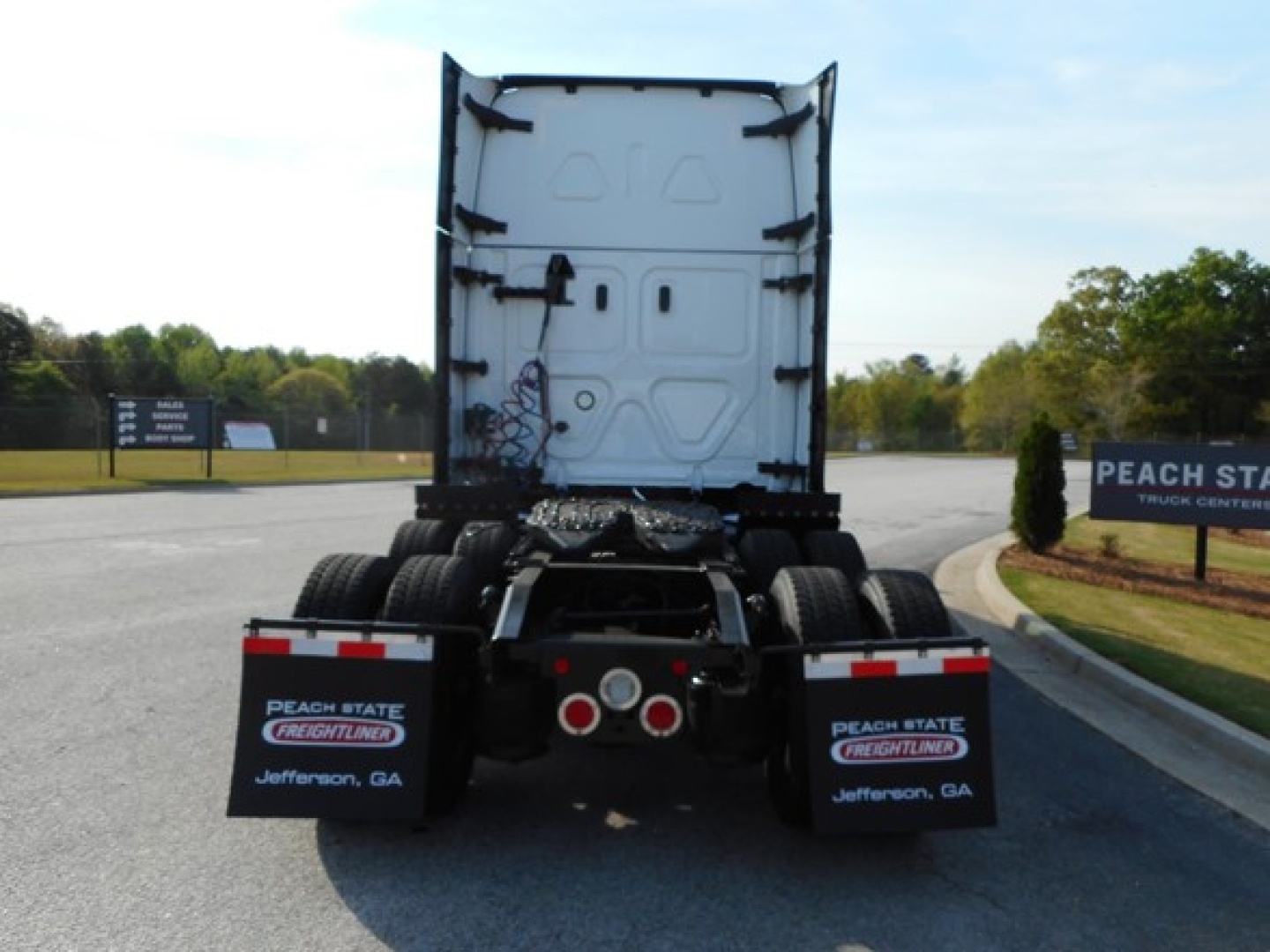 Rear view of a Freightliner tractor truck chassis showing dual rear axles and mud flaps with Peach State Freightliner branding Jefferson, GA.