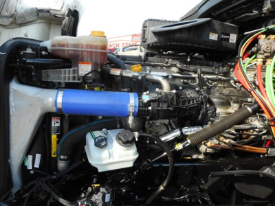 Tractor truck engine bay showing blue intercooler hose, coolant reservoir, and various wiring in a Freightliner Cascadia engine compartment.
