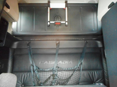 Freightliner Cascadia 126 sleeper interior cargo area with storage nets and lift mechanism showing rear wall and belts.