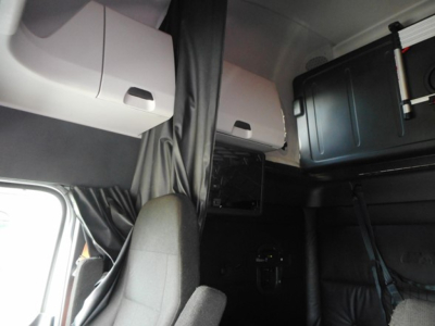 Cab interior of a Freightliner Cascadia sleeper showing upper storage cabinets and a hanging curtain.