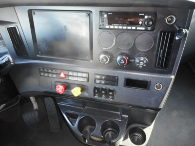 Cabin dash of a Freightliner Cascadia showing stereo, circular gauges, climate controls, hazard button, and cup holders.