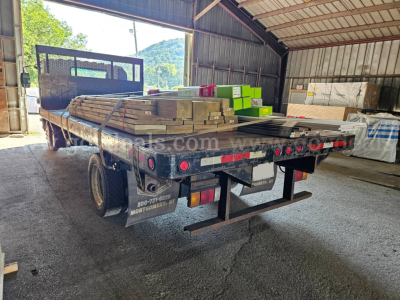 Isuzu NQR dump truck bed with lumber and materials loaded on flatbed, rear view inside a warehouse.