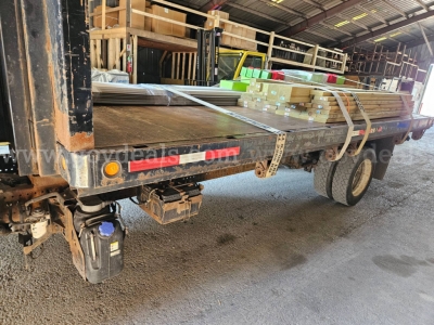 Isuzu NQR dump truck bed showing rear and side with stacked lumber and pallets; VIN JALE5W169G7301492 visible; stock number 32136-91; various equipment accessories under bed.