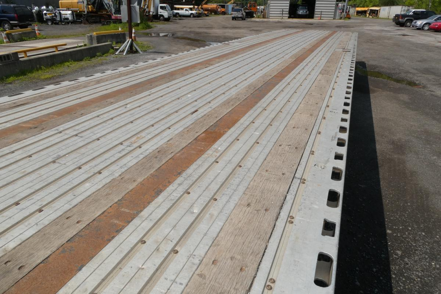 Flatbed trailer deck showing long metal planks and edge perforations with wood accents in a lot.