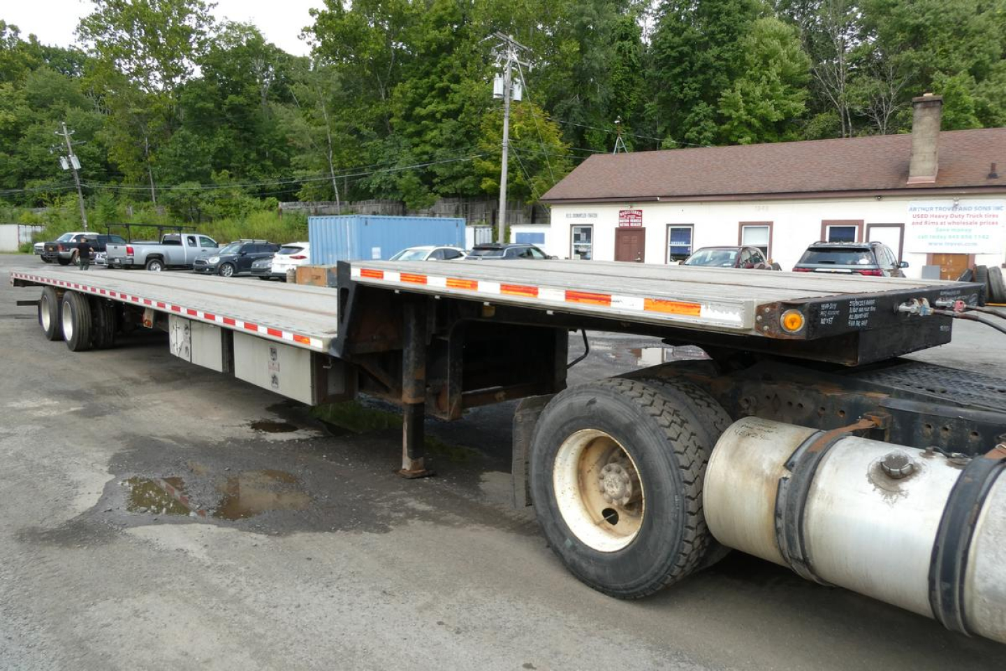 Flatbed trailer with dual rear axles and propane tanks, showing long deck and side markings, Fontaine HCITX22RSA model label on front corner.
