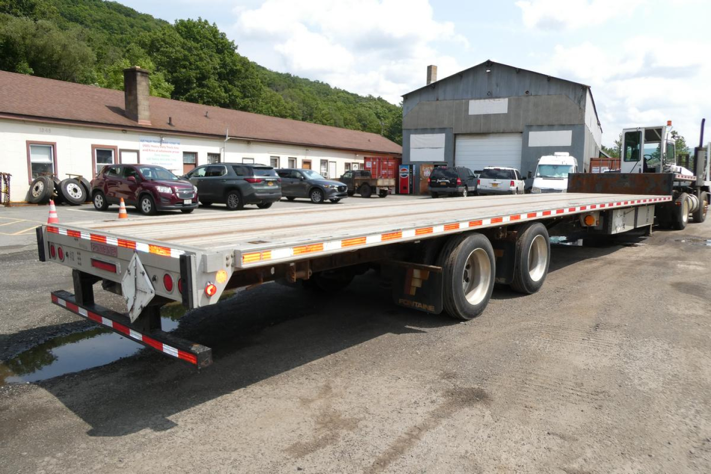 Flatbed trailer with triple-axle undercarriage and reflective safety markings, Fontaine HCITX22RSA model in a yard.