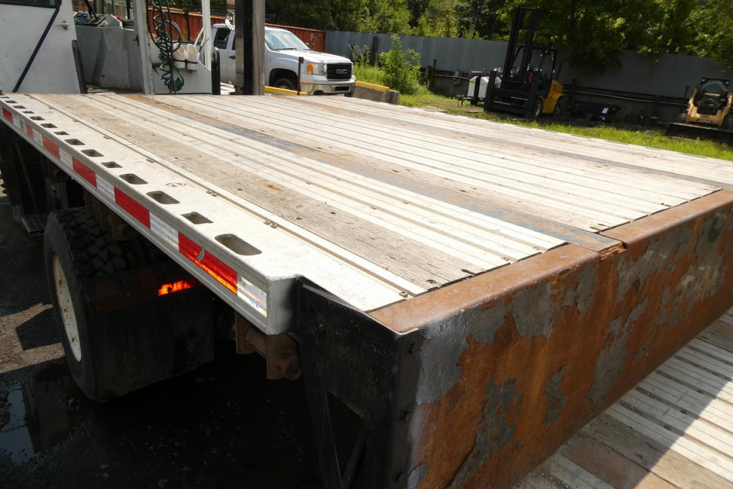 Flatbed trailer deck showing weathered aluminum planks and rusted steel frame with orange-brown rust on the endpost