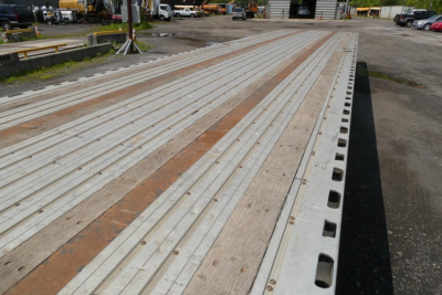 Flatbed trailer deck showing long metal planks and edge perforations with wood accents in a lot.