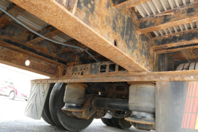 Trailer undercarriage showing rusty steel frame and axles with air springs and tires visible under deck.