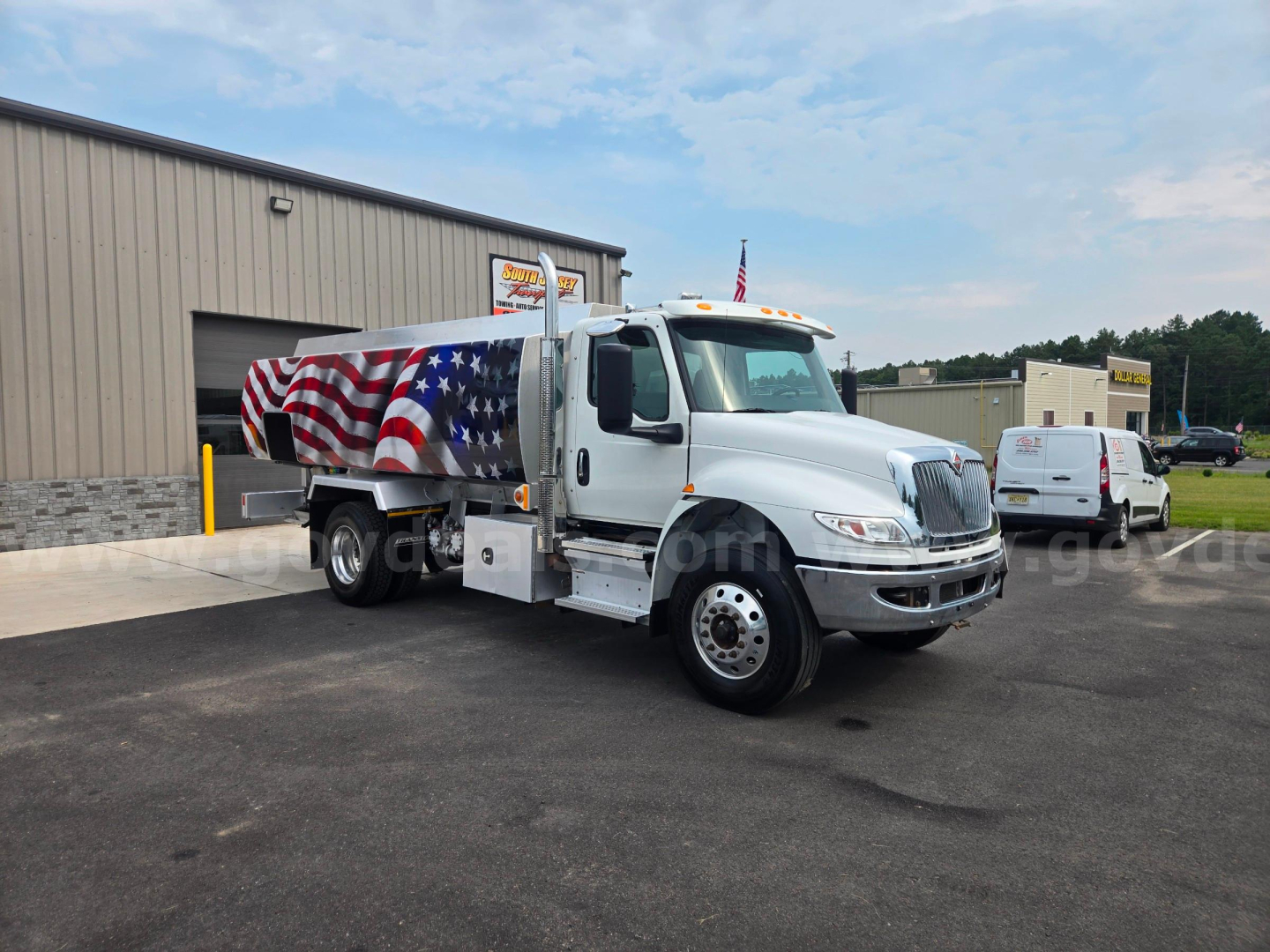 Truck with patriotic paint on a fuel tanker, International logo on front, American flag design on tank, shows side of cab and tanker with wheel, outdoor lot.