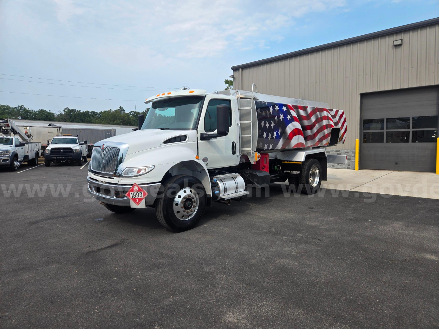 International fuel tanker truck in white with an American flag wrap, front view angled left, stock number 29174-90, industrial building in background