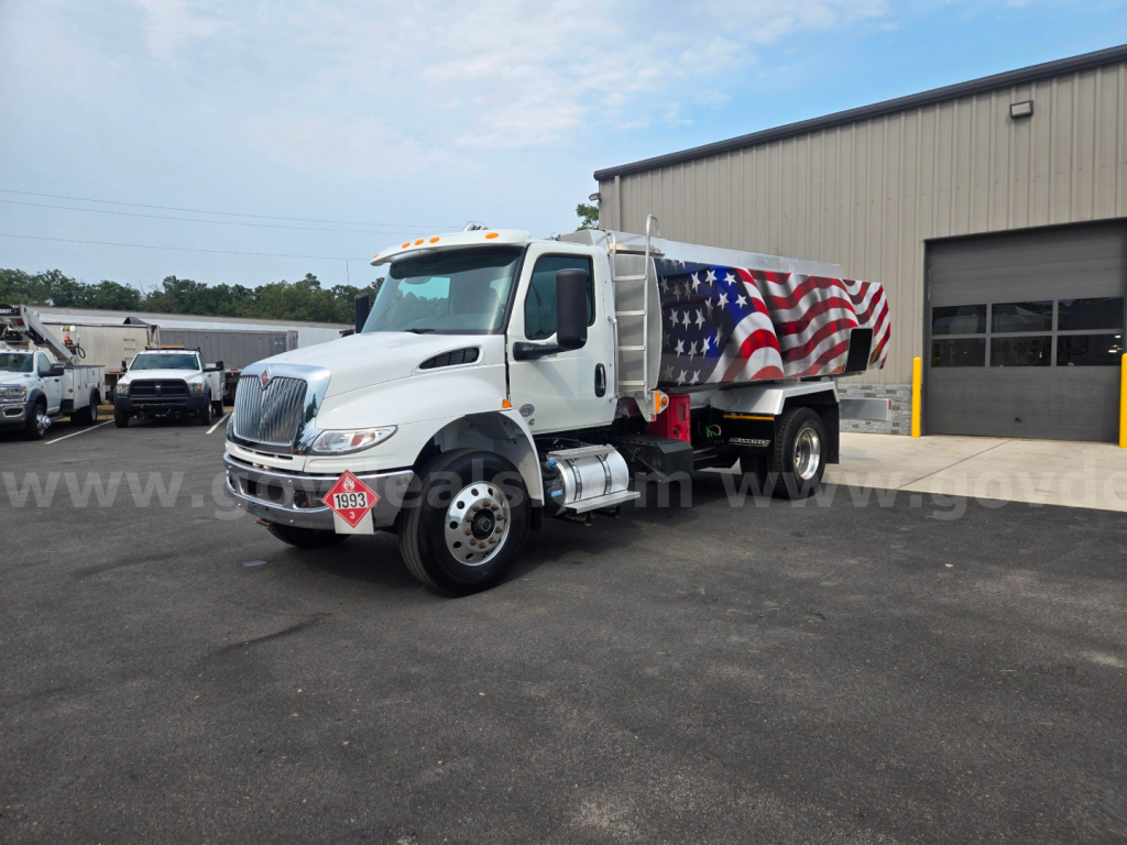International fuel tanker truck in white with an American flag wrap, front view angled left, stock number 29174-90, industrial building in background