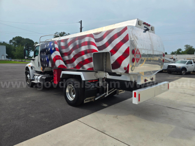 Truck-mounted fuel tanker with an American flag paint scheme, rear view showing tank, rear bumper, and warning placards.