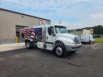 Truck with patriotic paint on a fuel tanker, International logo on front, American flag design on tank, shows side of cab and tanker with wheel, outdoor lot.
