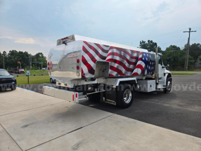 Truck-mounted fuel tanker with red white and blue American flag design on tanker body, rear loading ramp extended, International truck cab.