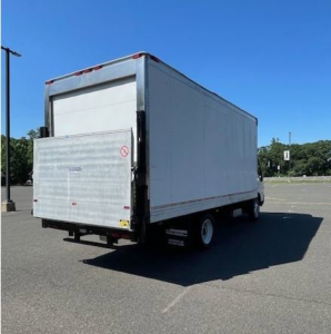 Truck rear view showing a white box van with a liftgate in a parking lot.