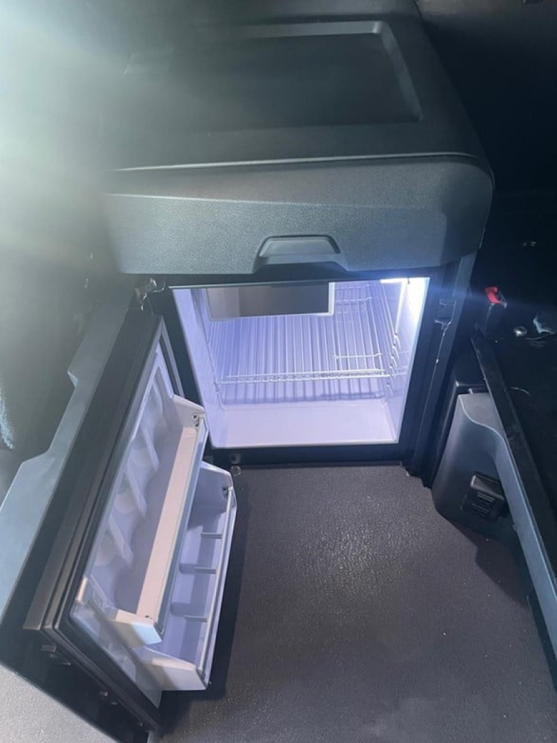Fridge/freezer of a Freightliner Cascadia sleeper cab showing open mini fridge with shelves and interior light.