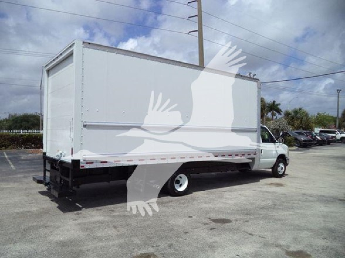Box truck rear side view showing large cargo box on a Ford E450 with white exterior and black chassis, street scene in background.