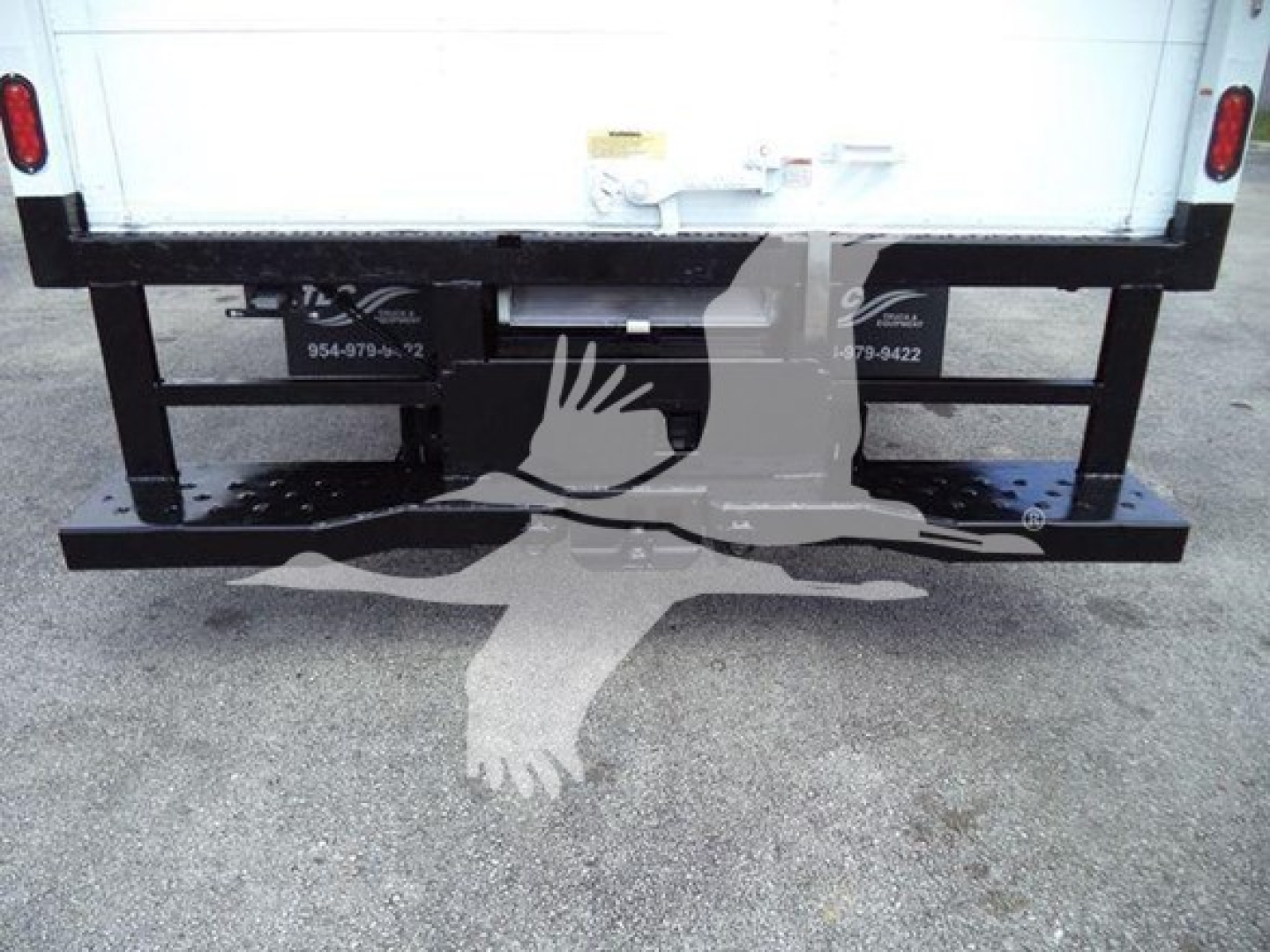 Rear view of a truck box with a heavy-duty black bumper/step. Visible stickers show numbers and labels on the undercarriage.