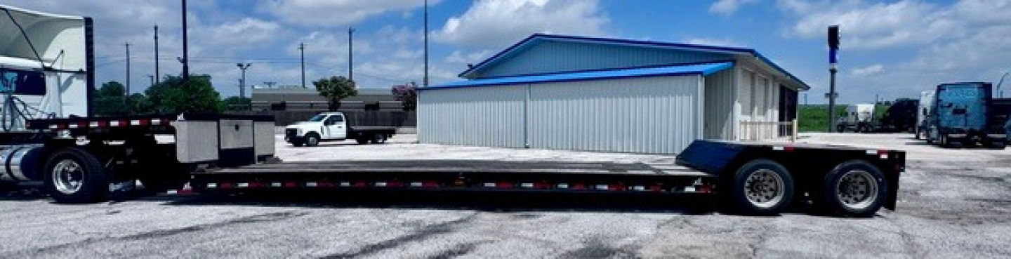 Lowboy trailer showing long flatbed with dual rear axles and gooseneck hitch area visible
