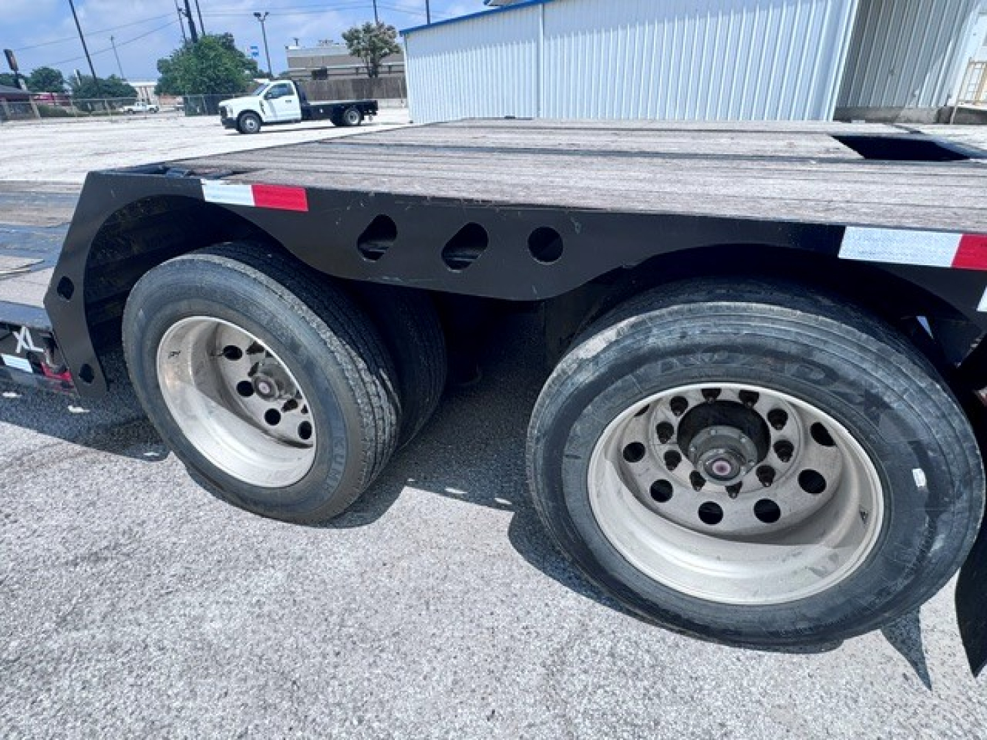 Trailer wheel area showing dual axles with tires and rims on a lowboy trailer. Visible text includes no specific labels in the wheel area.