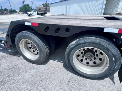 Trailer wheel area showing dual axles with tires and rims on a lowboy trailer. Visible text includes no specific labels in the wheel area.