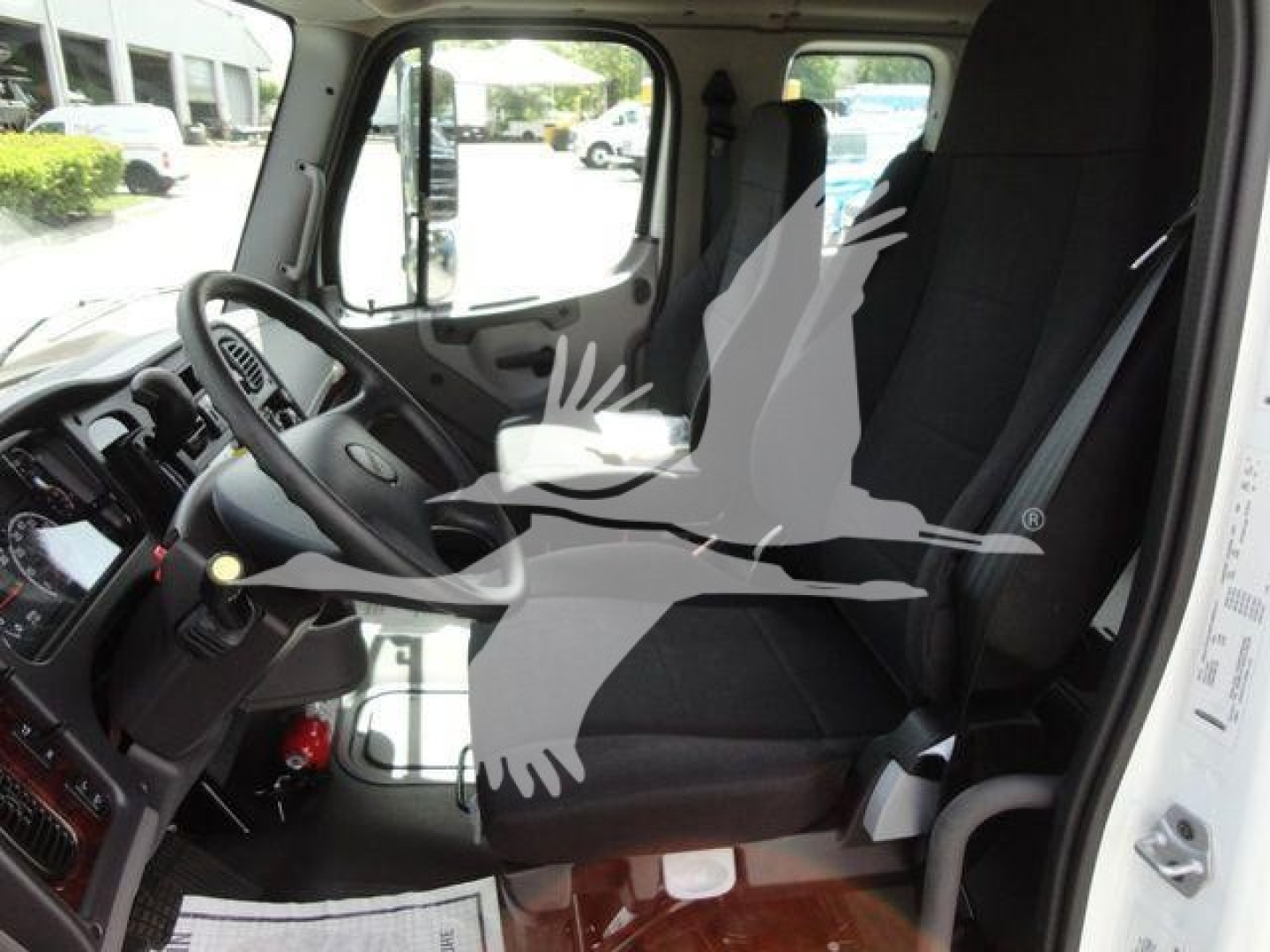 Truck cockpit view of a 2027 Freightliner Business Class M2 showing driver seat, steering wheel, dashboard, and front passenger seat.