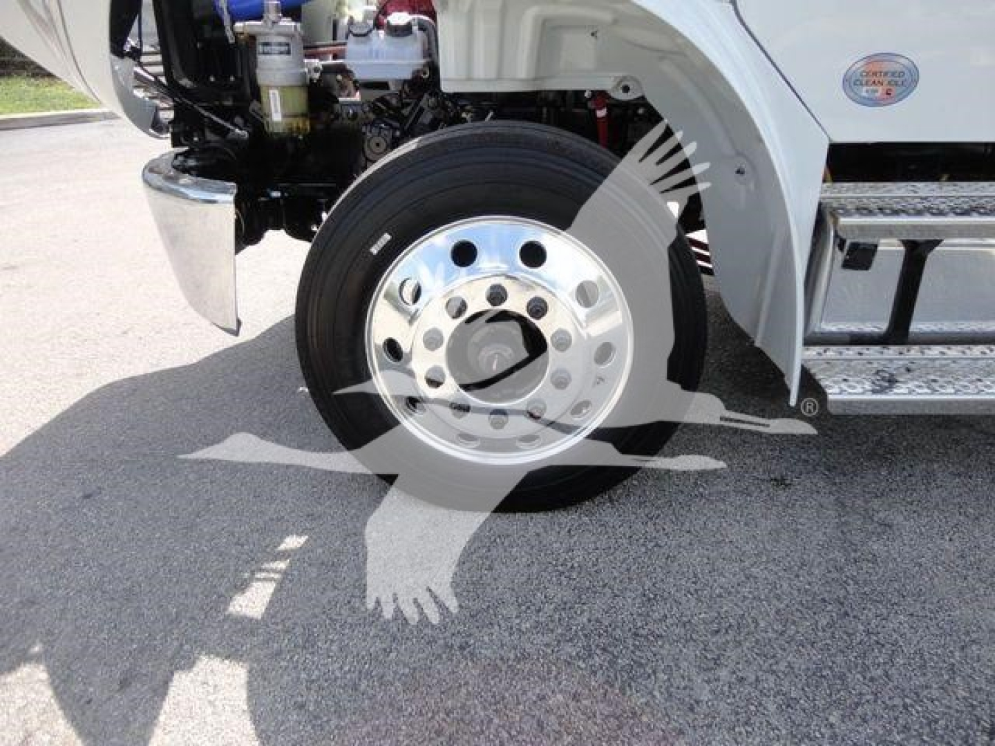 Truck front wheel assembly and partial cab area of a Freightliner Business Class M2 rollback truck showing chrome wheel, tire, and lower body components.