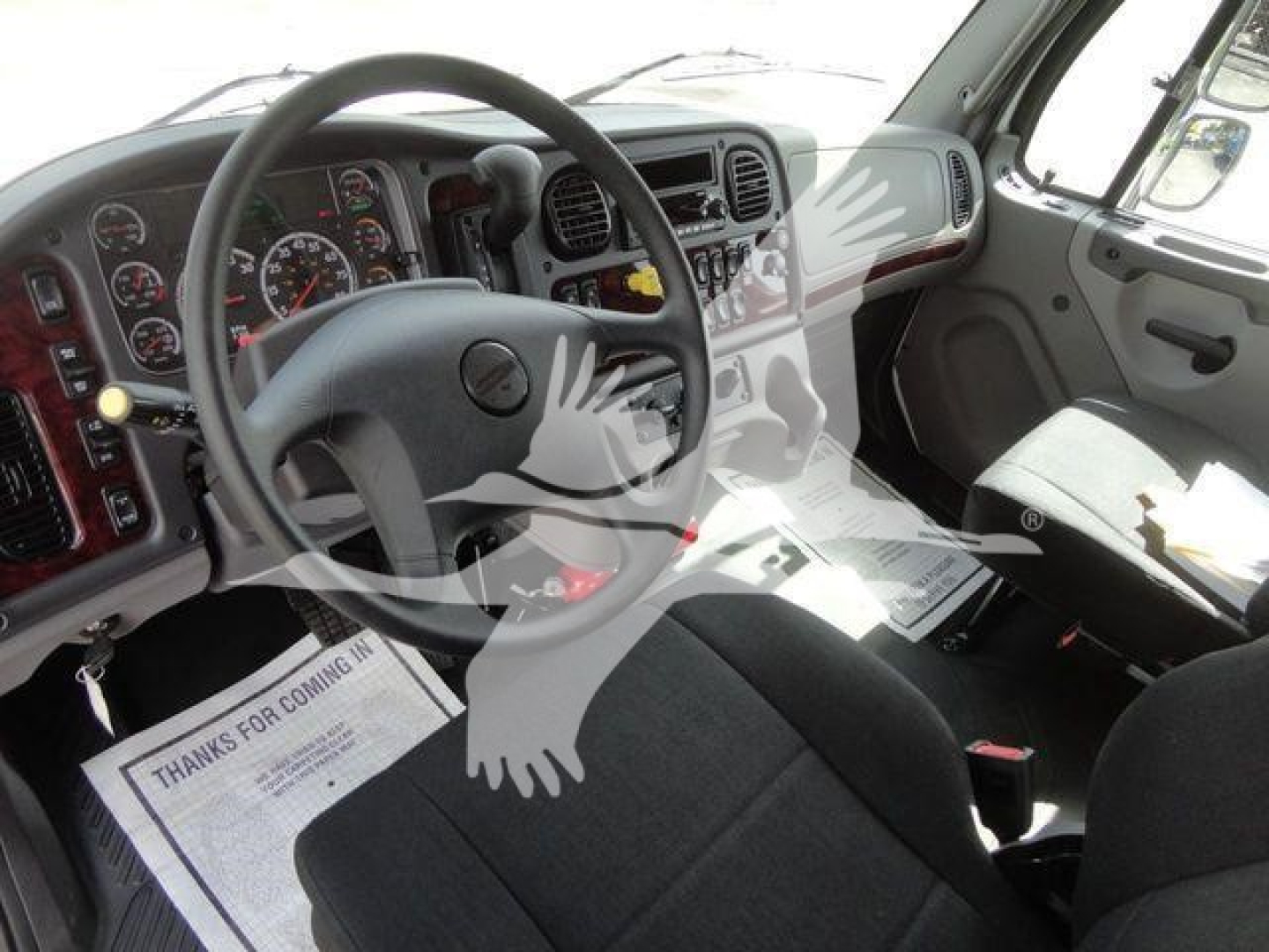 Interior view of a Freightliner Business Class M2 cab showing steering wheel, dashboard with gauges, and driver and passenger seats.