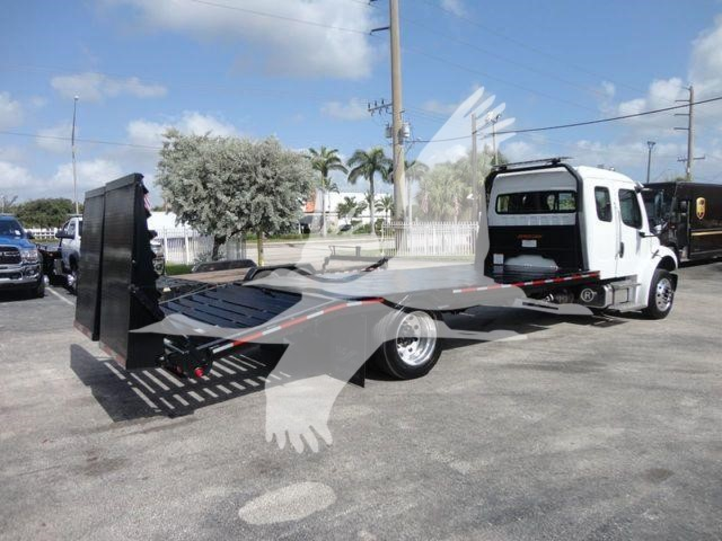 Flatbed tow truck with a rollback bed extending from the cab, Freightliner Business Class M2 style truck in light color, side view.