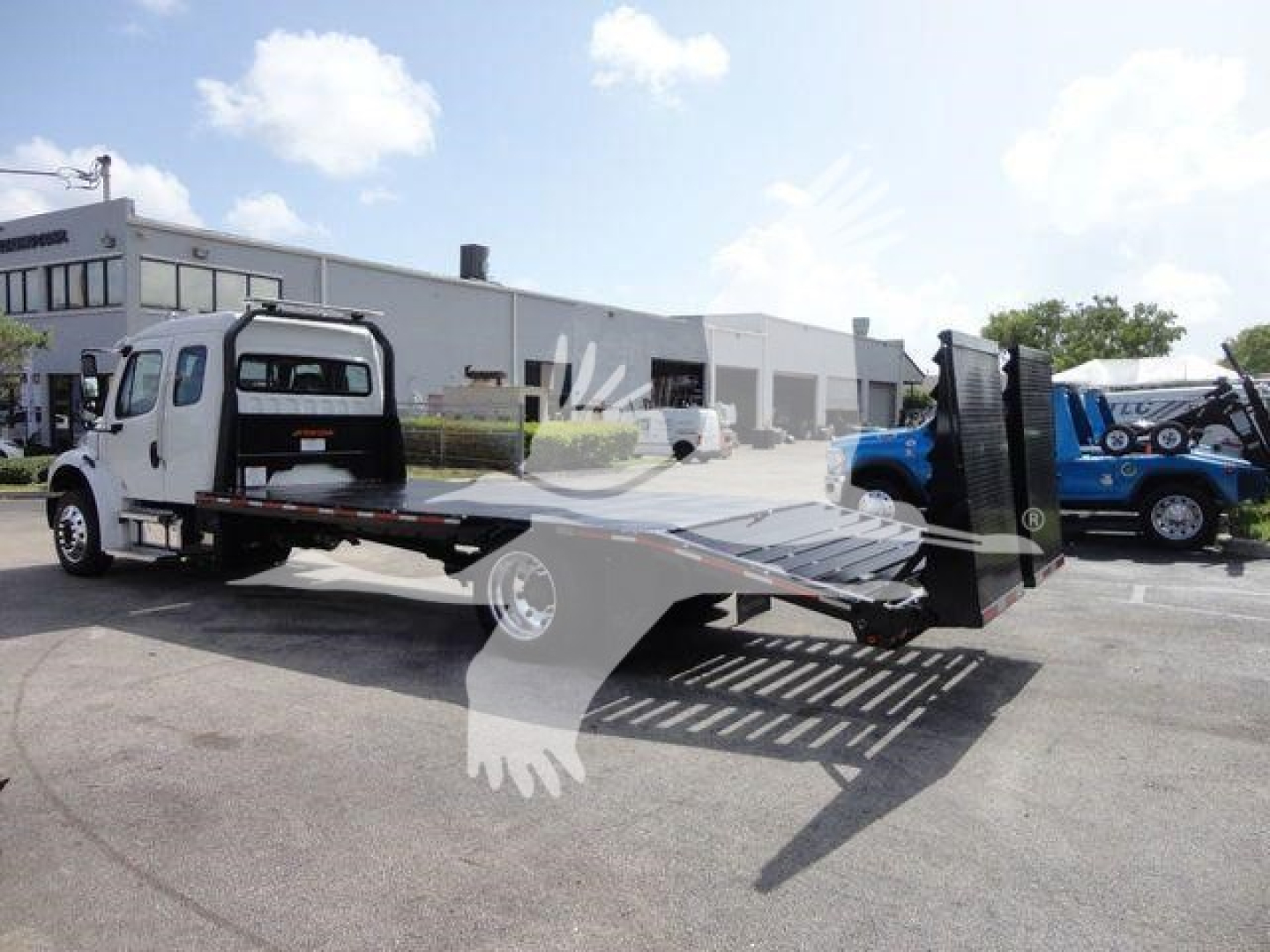 Truck with a flatbed rollback disabled view showing Freightliner Business Class M2 chassis and loading bed in a dealership lot.