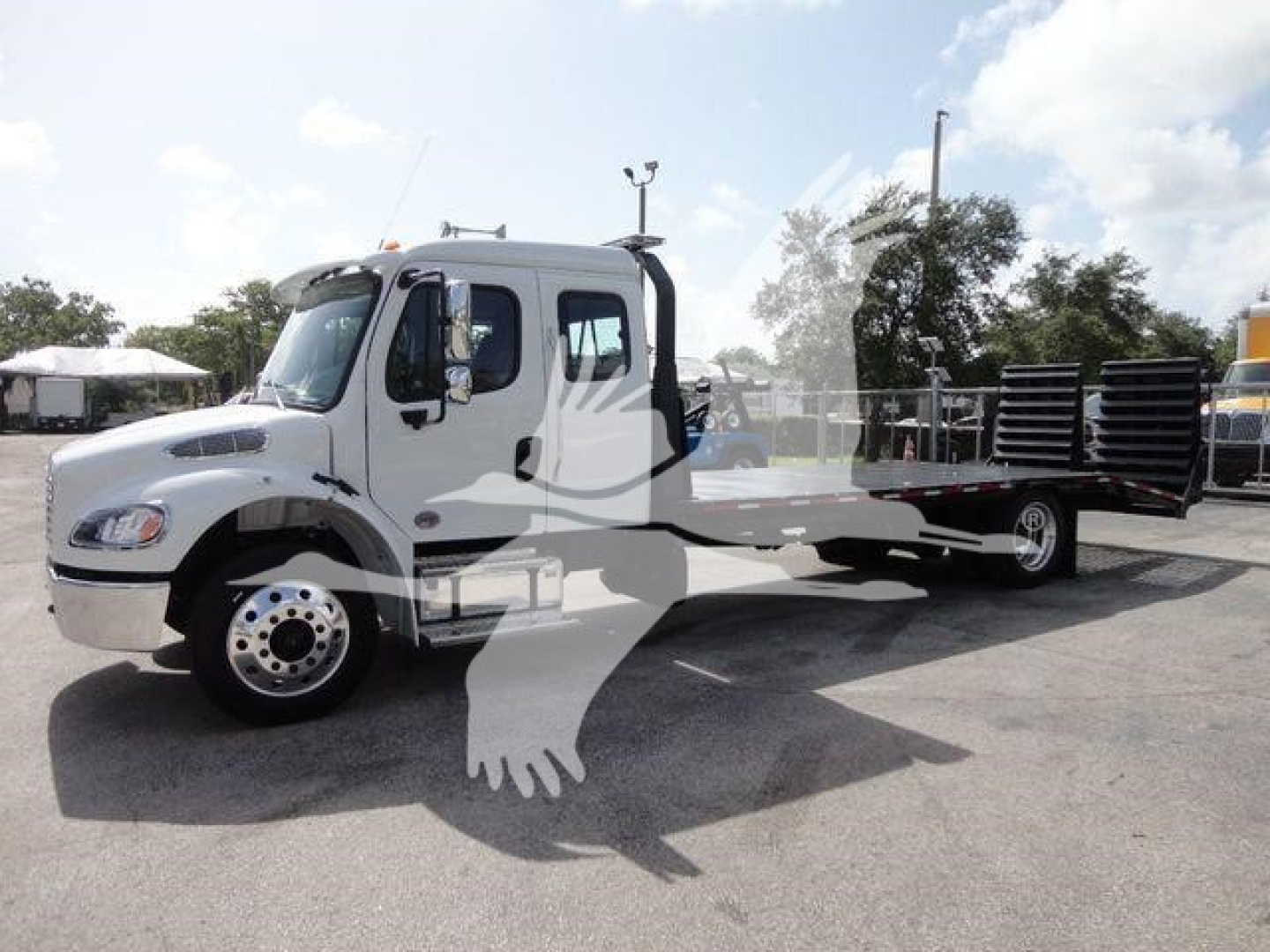 Freightliner Business Class M2 rollback truck in a dealership lot, white cab, flatbed with loading equipment visible.