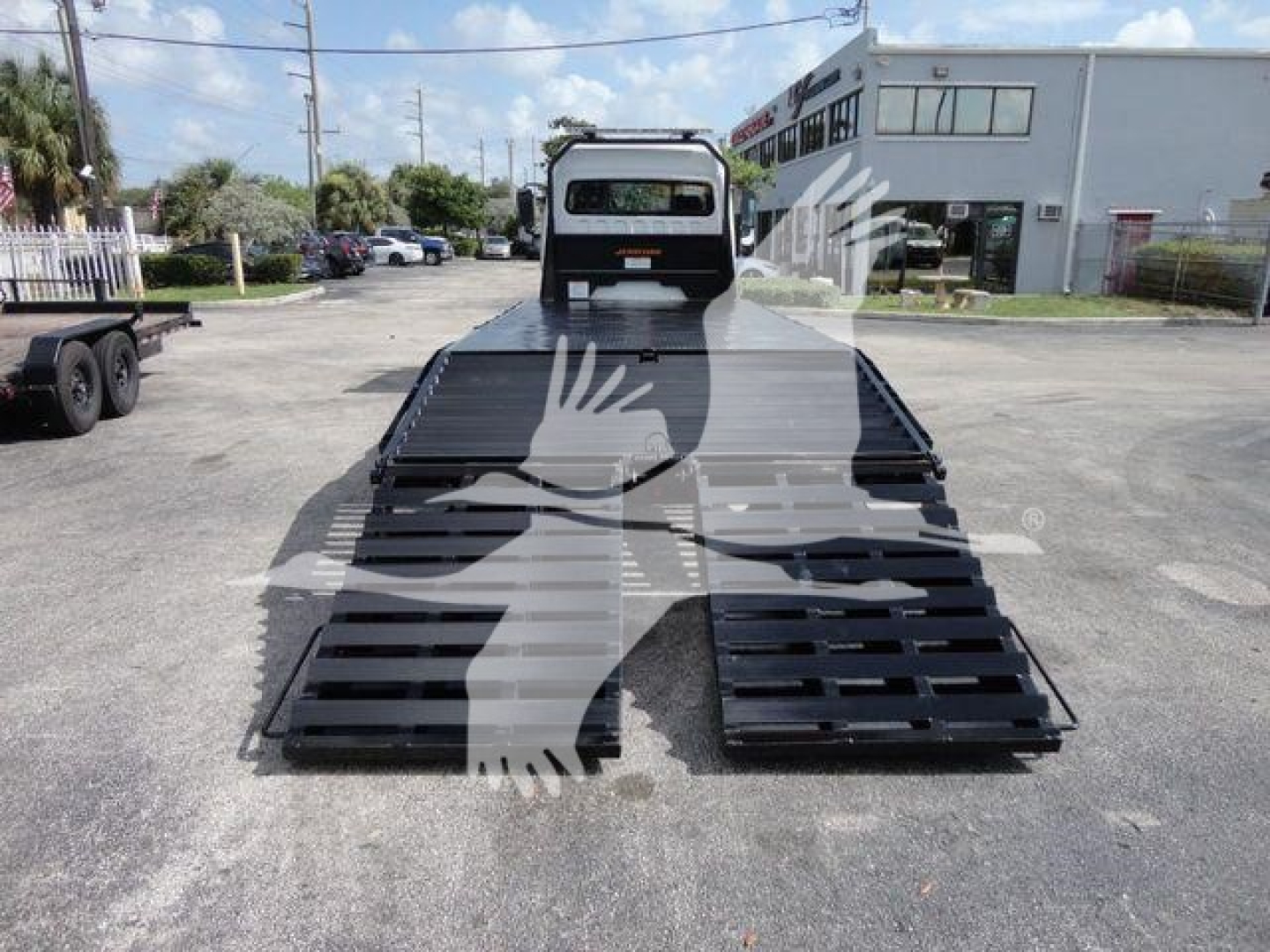 Freightliner Business Class M2 rollback truck in a lot with a low-profile flatbed ramp system extended, rear view with cab in distance.