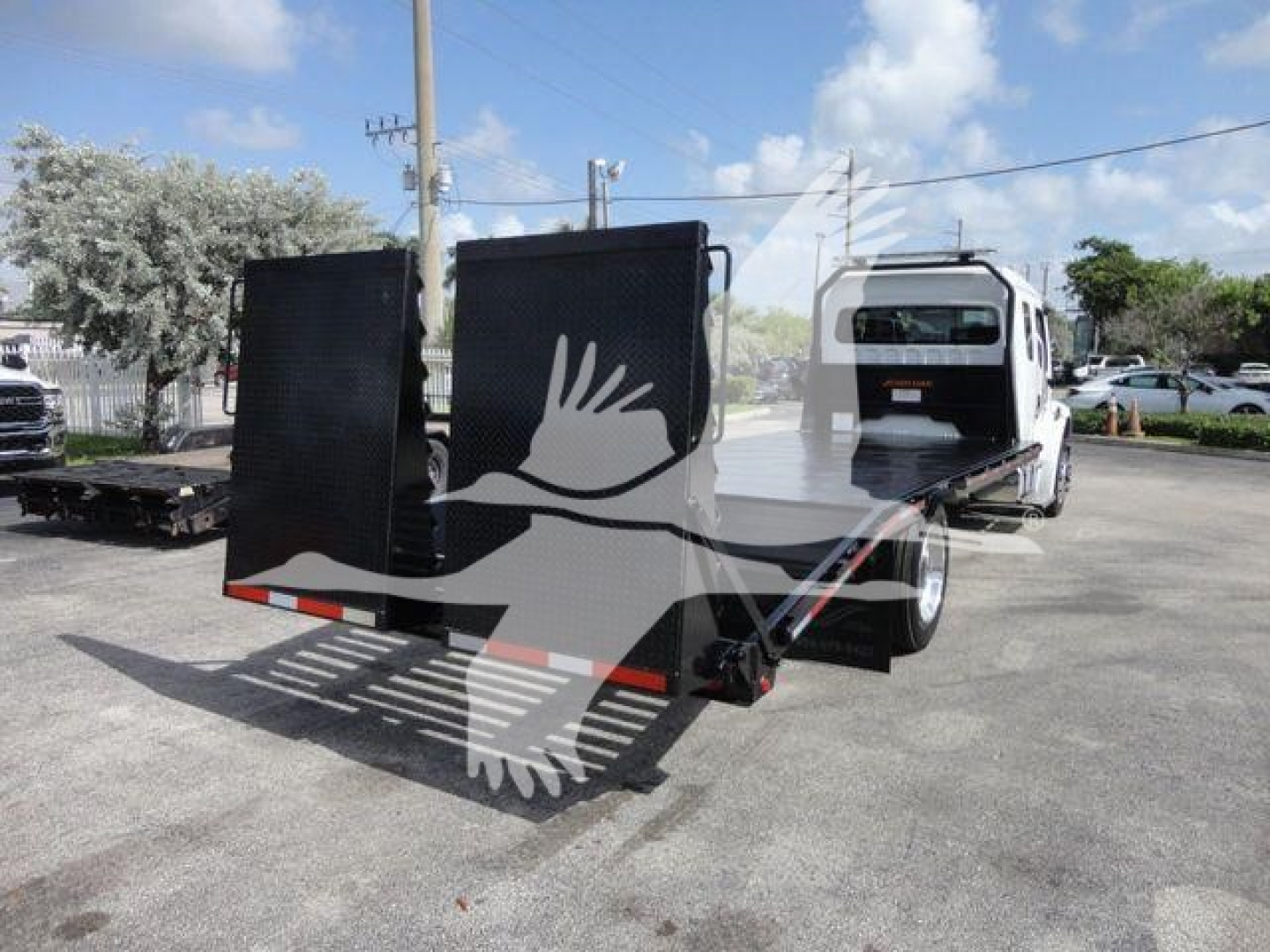Freightliner Business Class M2 rollback truck with a flatbed and a hinged cargo bed in a dealership lot.