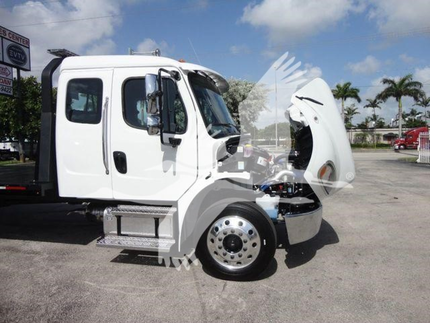Freightliner Business Class M2 truck with hood open, side view showing front wheel and cab, in a dealership lot.