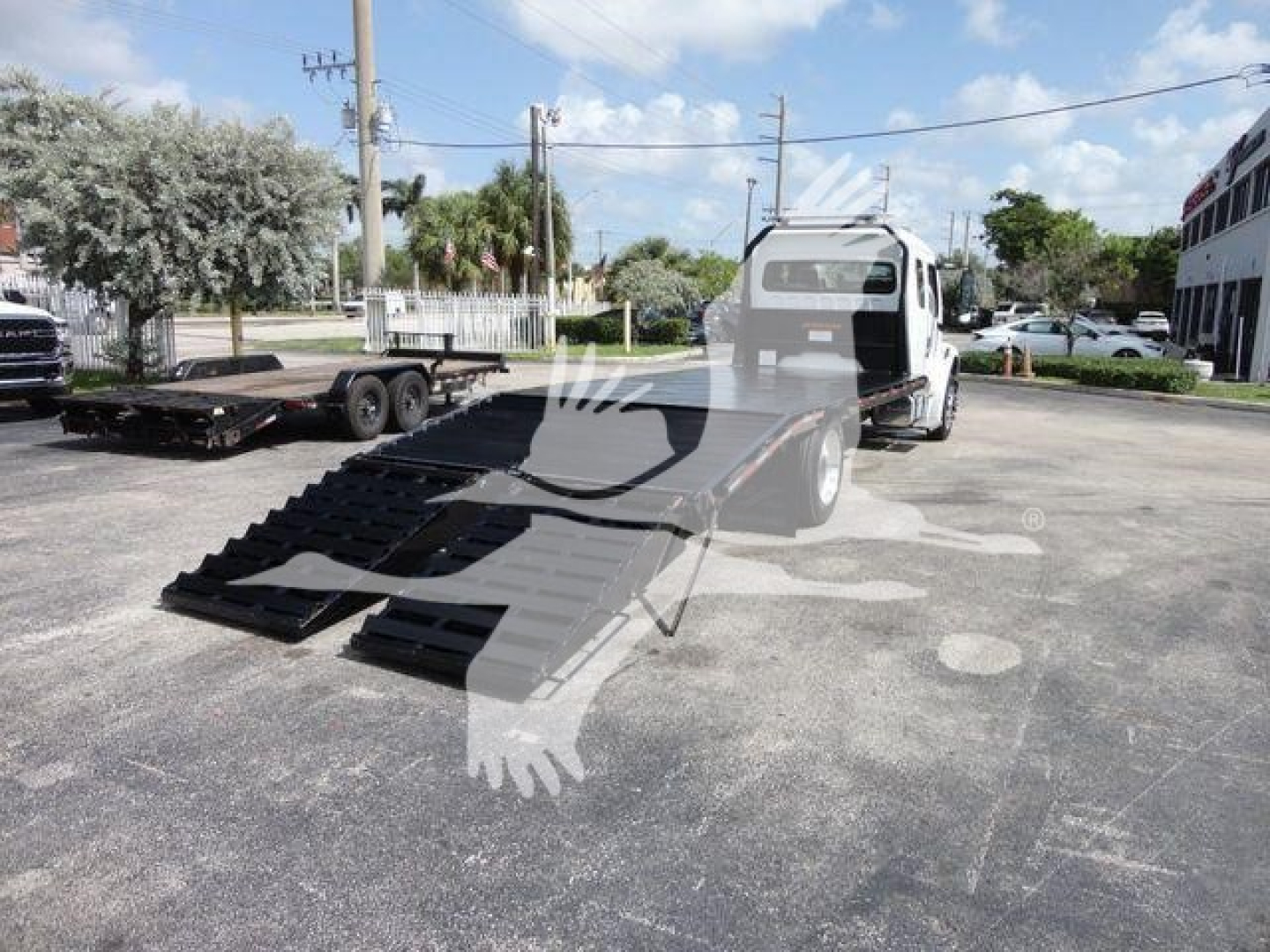 Truck with a flatbed rollback, loading ramps extended, Freightliner Business Class M2 cab visible in background.
