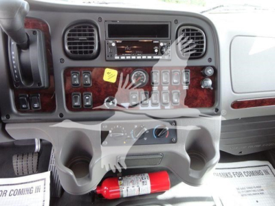 Dashboard view of a Freightliner Business Class M2 cockpit showing center console with numerous switches, vents, infotainment, and cup holders; red fire extinguisher mounted below.